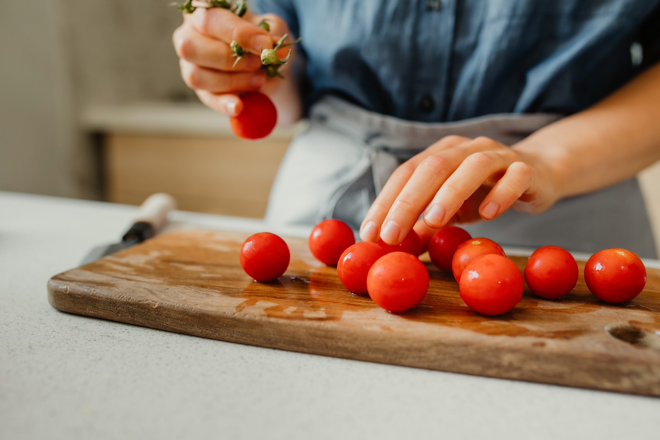 A person wearing an apron, preparing cherry tomatoes for cooking.